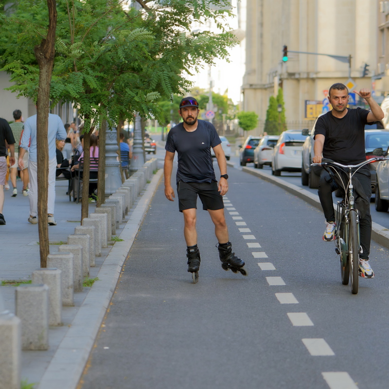 20 - Man wearing a blue shirt and black shorts rollerblading down a city street in the middle of a dedicated bike lane